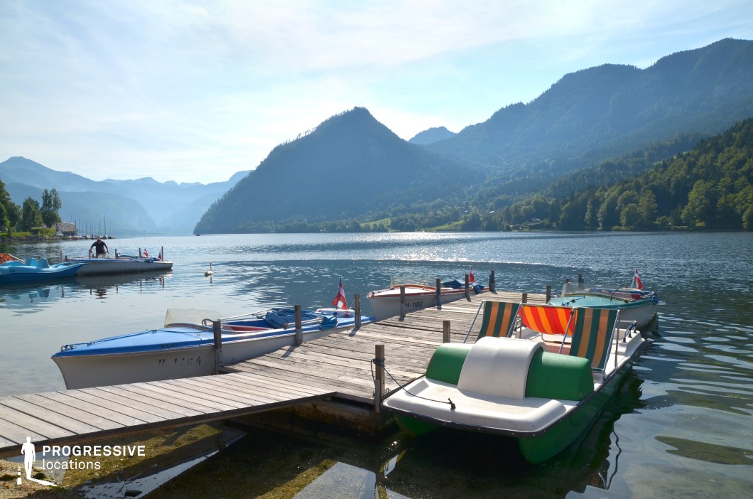 This peaceful lakeside dock extends into a shimmering alpine lake, surrounded by forested slopes and distant mountain ridges. The calm water, moored pedal boats, and layered mountain backdrop give the setting a relaxed, idyllic charm. The combination of leisure and natural grandeur makes this location ideal for filming summer vacation scenes, romantic moments, introspective retreats, or lighthearted comedies and dramas set in a scenic resort town.