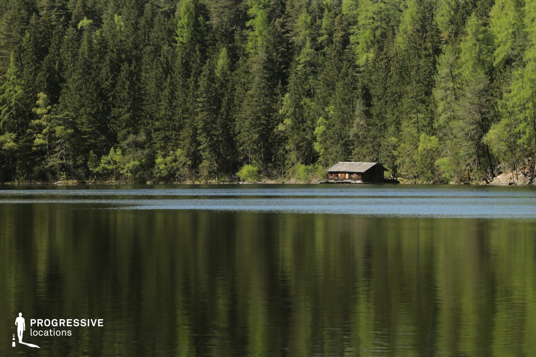 This secluded setting features a solitary wooden cabin nestled at the edge of a still lake, surrounded by dense, towering pine trees reflected in the water’s surface. The deep greens and natural symmetry create a sense of isolation, peace, and mystery, making it a visually powerful and emotionally evocative location. Perfect for psychological thrillers, nature-based dramas, or fantasy films, this spot is ideal for scenes involving retreats from society, hidden dwellings, quiet revelations, or eerie solitude deep within the wilderness.