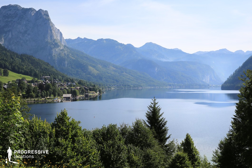 This panoramic location captures a serene alpine lake bordered by steep, densely forested slopes and dominated by towering mountain ridges in the background. The tranquil water surface mirrors the surrounding landscape, while the small lakeside village adds a touch of scale and rustic charm without overpowering the natural setting. The vastness and layering of mountains, trees, and water offer excellent depth for cinematic compositions. This location is ideal for fantasy epics, romantic dramas, or travel-themed productions—especially scenes of arrival, reflection, or majestic overviews of a character’s journey through breathtaking terrain.