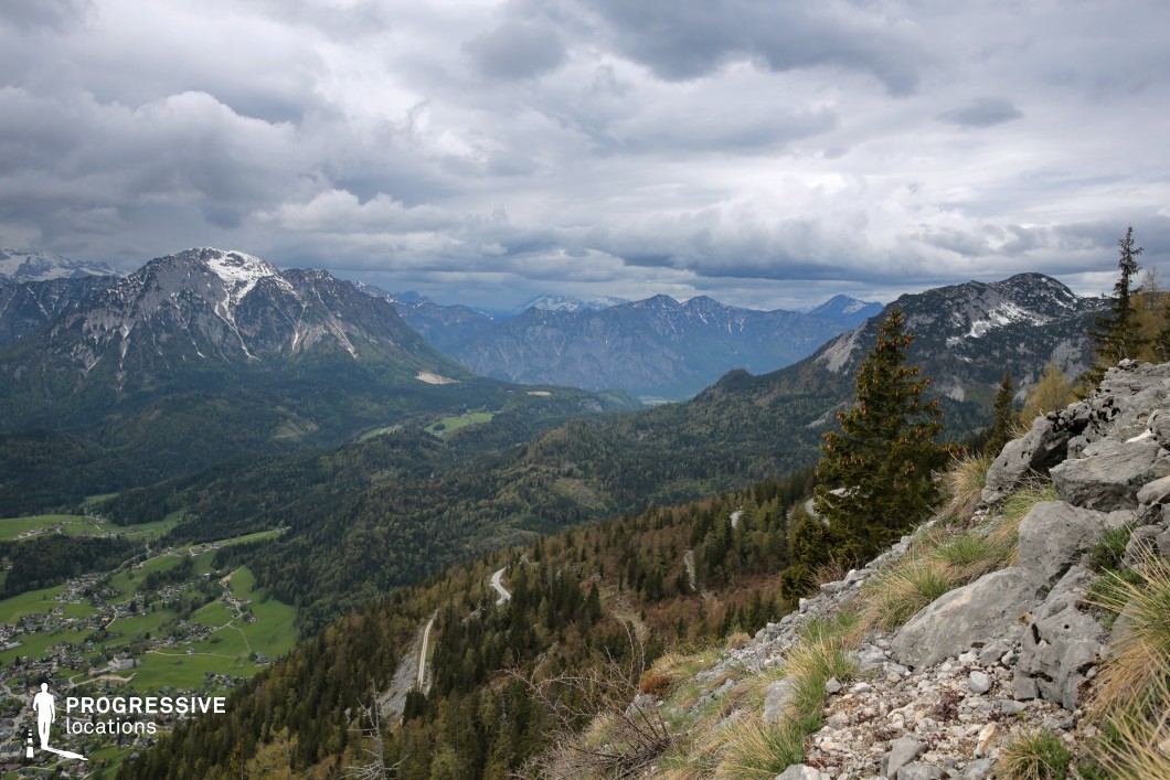 This panoramic vista captures a vast alpine landscape with rugged cliffs, deep forested valleys, distant snow-dusted peaks, and scattered villages nestled far below. The layered terrain and brooding cloud cover add tension and grandeur, making the scene visually rich and emotionally charged. Ideal for epic fantasy, historical journeys, or introspective adventure films, this location offers a powerful setting for moments of triumph, solitude, confrontation, or revelation.