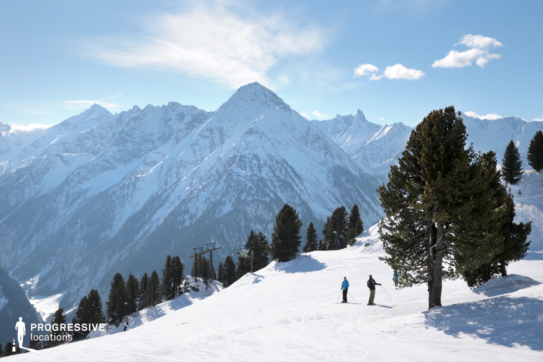 This striking mountain landscape features a dominant pyramidal peak surrounded by a range of jagged alpine summits, all blanketed in snow. The composition is defined by strong diagonal lines formed by the ridges and valleys, offering excellent depth and perspective. The expanse of the white terrain contrasts with the forested lower slopes, while the infrastructure of a ski lift introduces a subtle man-made element, blending into the natural surroundings. This location is ideal for filming high-altitude scenes and offers great potential for adventure, thriller, or drama genres. It would work especially well for action sequences, winter sports montages, or reflective, solitary character moments.