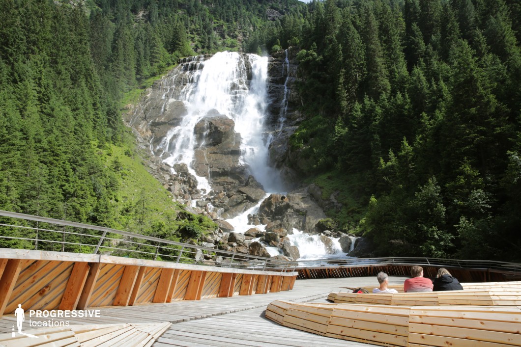 This expansive wooden platform with built-in seating opens toward a powerful multi-tiered waterfall cascading down a forested mountainside. Surrounded by dense evergreen trees and steep rocky slopes, the viewing area blends modern design with the raw energy of nature. The symmetry of the benches and the central alignment of the falls create a visually striking focal point. This location is ideal for emotional turning points, nature documentaries, fantasy epics, or meditative sequences, offering a stunning natural backdrop for awe, reflection, or revelation.