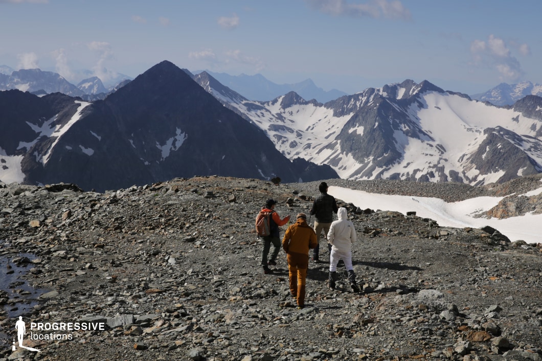 This high-altitude location features a dramatic rocky ridge overlooking a vast expanse of snow-draped mountains and sharp, jagged peaks. The rugged terrain, mixed with patches of snow and scree, conveys a raw and unforgiving landscape. The wide, unobstructed view allows for sweeping camera movements and cinematic depth. Ideal for epic adventure films, survival stories, or fantasy quests, this setting can serve as a pivotal transition point, a climactic journey scene, or a moment of awe and revelation at nature’s extremes.