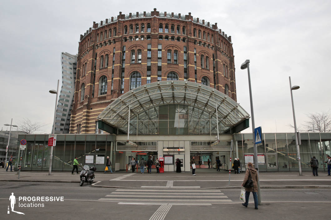 This visually striking location merges industrial heritage with contemporary urban infrastructure. The dominant feature is the massive circular brick structure, a former gasometer, showcasing intricate masonry, arched windows, and vertical architectural elements that convey a sense of history and grandeur. In contrast, the foreground features a modern glass and steel transit station with a curved, transparent roof, creating a dynamic blend of old and new. The juxtaposition of historic and futuristic design elements makes this an ideal setting for filming urban dramas, dystopian sci-fi, or historical retrospectives, offering a versatile backdrop that reflects both industrial past and modern transformation.