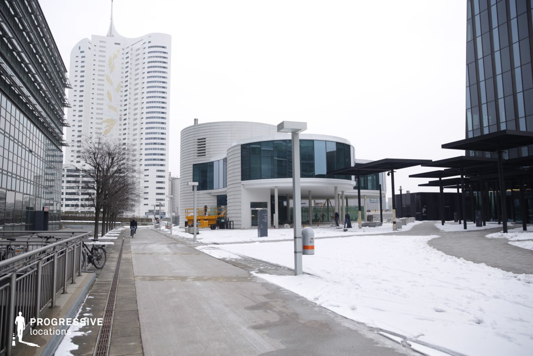This contemporary cityscape features a mix of sleek glass facades, curved architectural structures, and high-rise buildings, creating a dynamic and futuristic environment. The blend of geometric forms, from cylindrical low-rise constructions to towering skyscrapers, adds a layered depth to the setting. The use of reflective surfaces and minimalist black and white elements enhances the clean, professional atmosphere. Wide pedestrian walkways and strategically placed street lighting contribute to the area's functionality and accessibility. This location is ideal for corporate, sci-fi, or cyberpunk-style films, offering a versatile backdrop for business-centric narratives, high-tech espionage scenes, or urban futuristic storytelling.