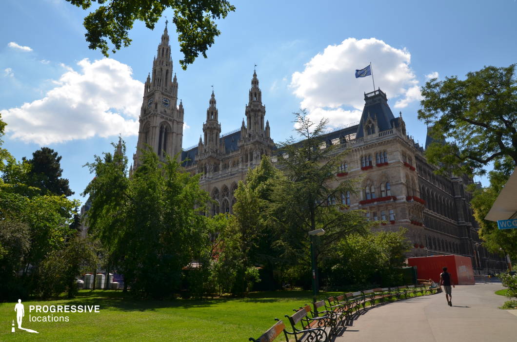 This striking location features an elaborate neo-Gothic building with towering spires, intricate stone detailing, and arched windows, exuding a grand and institutional character. The adjacent park provides a lush, open foreground with manicured green lawns, a winding pathway, and rows of classic iron-framed benches, creating a balanced contrast between nature and architecture. The building’s ornate façade, adorned with decorative balconies and flags, adds a regal and historic atmosphere, while the surrounding trees frame the scene naturally. This location is ideal for filming political dramas, historical pieces, or sophisticated urban scenes, offering both an imposing civic backdrop and a tranquil public space for diverse storytelling needs.