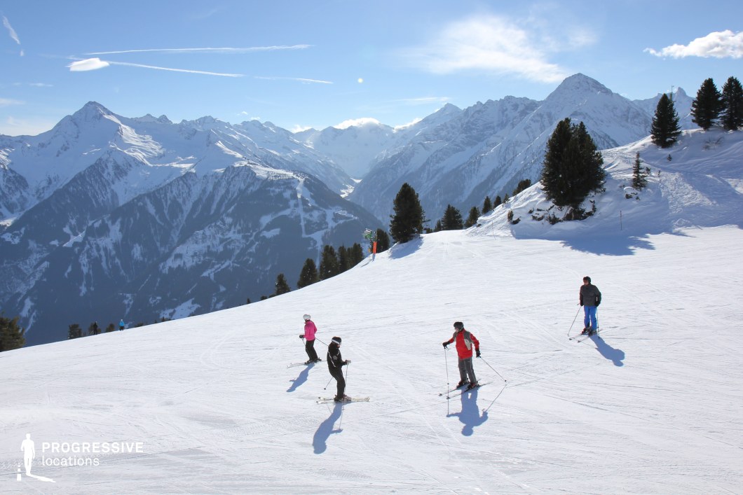 This location features a wide, gently sloping snow-covered terrain situated in an expansive alpine environment, framed by a dramatic backdrop of towering, rugged mountain ranges. The slopes are flanked by clusters of evergreen trees, adding vertical texture and a natural rhythm to the landscape. The pristine white snow contrasts sharply with the deep green of the trees and the dark ridgelines of the surrounding peaks, creating a clean, high-contrast visual aesthetic. The mountains in the background exhibit sharp angular formations and varying elevations, contributing to a layered sense of depth and grandeur. The camera angle is set from an eye-level perspective looking slightly downhill, which emphasizes the openness and natural flow of the terrain. This location is highly suitable for filming outdoor sequences requiring a majestic, remote, or adventurous atmosphere. It is ideal for genres such as action, drama, and documentary, particularly scenes involving alpine exploration, winter sports, or high-altitude solitude.