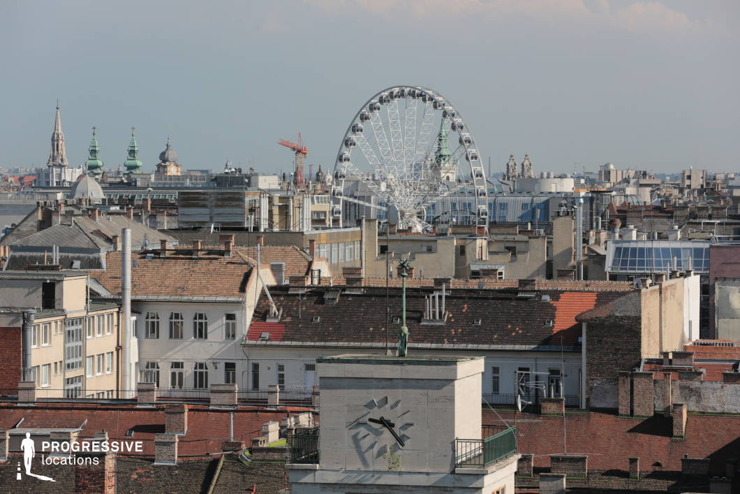 This image showcases a dynamic rooftop view of the city, with a mix of historical and modern elements. In the foreground, rooftops with traditional tiles and industrial chimneys create a textured urban landscape. Prominently featured in the background is a Ferris wheel, contrasting with the historical architecture of churches, each with distinct towers and domes, adding vertical interest to the scene. The city’s skyline stretches into the distance, blending old and new structures, including modern glass buildings and classic rooftops. This location offers a compelling juxtaposition of heritage and contemporary life, ideal for capturing the essence of a thriving urban environment. The scene is perfect for projects that explore the integration of cultural landmarks with modern development in an evolving cityscape.