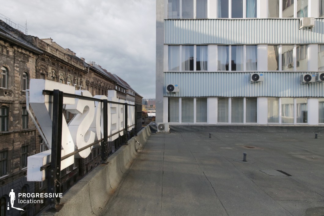 This image presents a contrast between modern and historical architecture, with a large, contemporary white sign positioned on a rooftop in the foreground. The sign, partially obscured by the building’s edge, overlooks a street lined with Soviet-era classical buildings, their weathered facades reflecting the passage of time. The building on the right features a modern, streamlined design with large windows and air conditioning units, adding a sharp contrast to the surrounding architecture. The scene captures the juxtaposition of old and new within an urban environment, where the contemporary signage interacts with the legacy of historic architecture. This view offers a compelling perspective for projects exploring the evolution of cityscapes, emphasizing the mix of styles and functions in an ever-changing urban landscape.