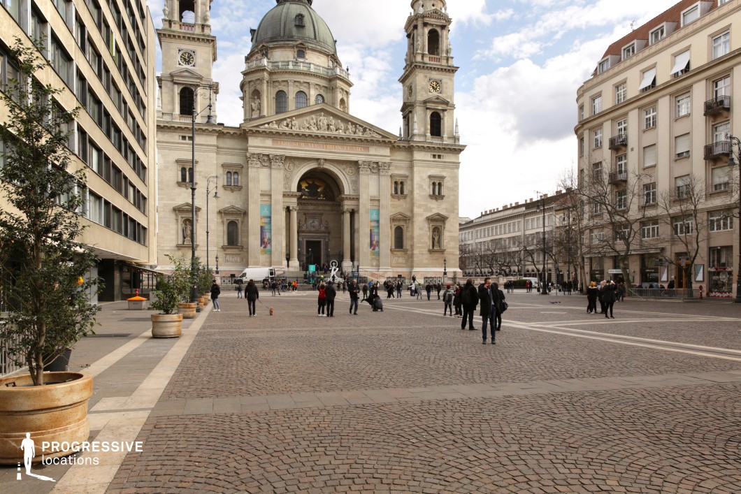 The image depicts a spacious, bustling urban square dominated by a grand neoclassical basilica in the background. 
