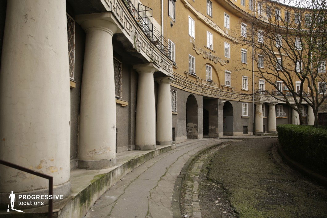This location showcases a blend of historicist and socialist realist architectural styles, featuring a semi-circular colonnade with massive classical columns and a weathered façade. The slightly worn decorations and faded yellow exterior create a nostalgic, authentic atmosphere, making it ideal for historical or post-apocalyptic film scenes as well as vintage-style fashion shoots. The geometric forms combined with natural elements, such as surrounding bushes and trees, provide a dynamic yet romantic visual experience. The courtyard, with its slightly abandoned yet elegant ambiance, makes this location a perfect choice for productions seeking an authentic and dramatic backdrop.
