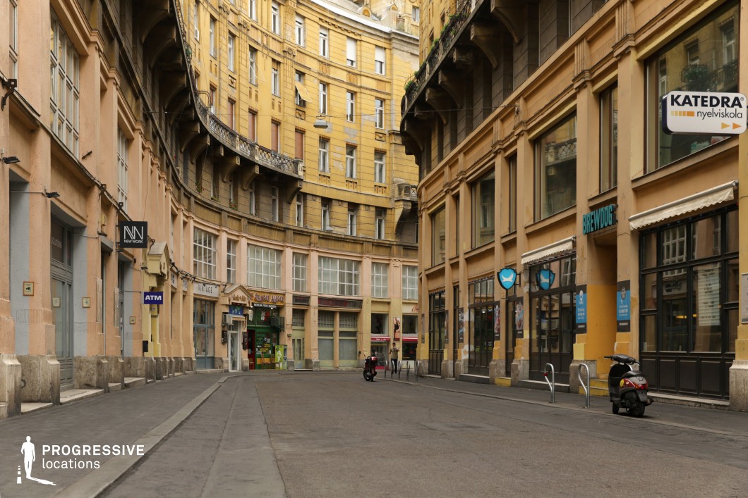 This image showcases a curved classical building façade, predominantly in muted yellow and beige tones, reflecting early 20th-century European urban architecture. The design features elegant balconies and large windows that follow the curvature of the street, creating a seamless sense of continuity and symmetry. The relatively narrow street, combined with the enclosed feel created by the bending perspective, makes this location particularly immersive, as the end of the road remains out of sight. The curved design of the building further enhances the dynamic nature of the setting, making it an ideal backdrop for scenes involving vehicles or pedestrians navigating urban spaces, creating a sense of motion or exploration. The muted tones of the façade add a classic and understated atmosphere, perfect for intimate or dramatic urban sequences.