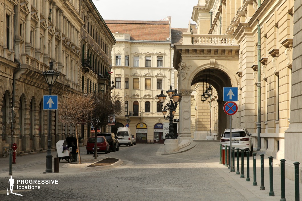 This location exudes a Parisian charm, with its elegant architecture, intricate details, and a distinct sense of history that creates an intimate, upscale urban atmosphere. The ornate archway with its spacious terrace above adds a layer of grandeur, providing an elevated architectural feature that enhances the sense of sophistication. Such terraces are not only visually striking but also evoke the elegance of historical European cities, serving as a reminder of classical architectural traditions.

The cobblestone paving, paired with the cast-iron street lamps, enhances the traditional European aesthetic, evoking a timeless sophistication. The lamps' intricate design and dark finish perfectly complement the pale stone facades and create a harmonious balance within the setting.

The street's layout provides a visually enclosed urban space, as the buildings, the terrace, and the archway naturally frame the view from all directions. This makes the location ideal for capturing cinematic moments where the focus remains on the immediate surroundings, free from visual distractions of open landscapes.

Perfect for fashion shoots, period dramas, or high-end commercials, this site offers a completely contained downtown setting with Parisian elegance, ensuring every angle delivers a cohesive, visually rich composition. The grand terrace above the archway further adds a touch of exclusivity, making the location stand out as a prime example of European urban beauty.