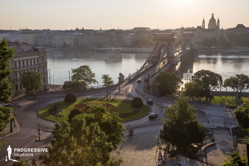 This panoramic view showcases a historic European bridge, gracefully spanning the Danube River and framed by a beautifully landscaped roundabout in the foreground.