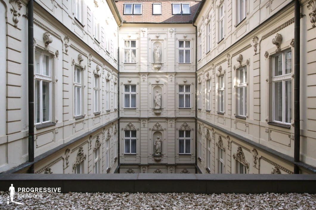 This pristine classical courtyard is enclosed by symmetrical white facades adorned with ornate stucco details, sculpted reliefs, and decorative window frames. The carefully arranged niches house graceful statues, reinforcing the building’s refined and aristocratic character. The soft natural light enhances the depth of the space, drawing attention to the perfect alignment of the architecture. This location is well-suited for period dramas, historical narratives, or sophisticated thrillers, providing a setting that conveys prestige, opulence, and a timeless European ambiance.