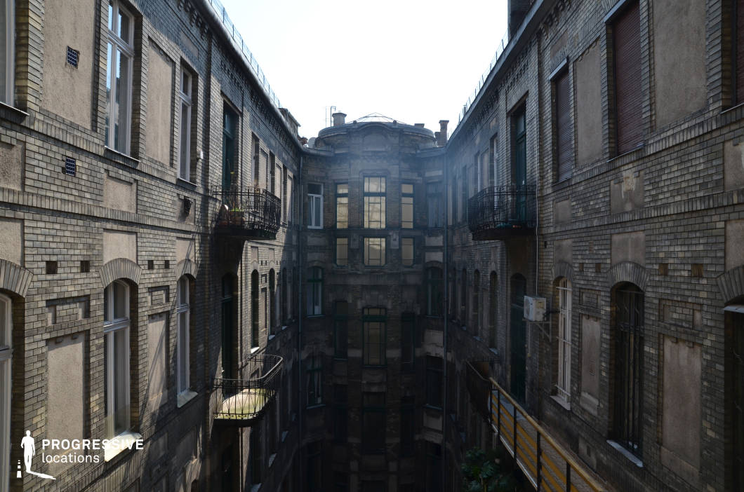 This imposing enclosed courtyard features tall, dark brick facades lined with arched windows and small wrought iron balconies, creating a striking, almost theatrical atmosphere. The symmetrical design and receding perspective draw the eye toward the central structure, which has large reflective windows and a rounded rooftop element, adding an air of mystery. The aged surfaces, subtle architectural details, and industrial-style railings contribute to the building’s austere, historical character. This location is ideal for filming noir thrillers, urban mysteries, or period dramas, offering a dramatic and enclosed setting that evokes secrecy, tension, and a sense of urban decay.