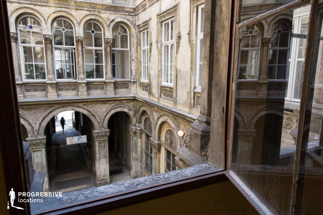 This weathered neoclassical courtyard, viewed from an aged open window, features a series of arched walkways, tall windows with decorative moldings, and faded facades that tell a story of forgotten grandeur. The intricate stone detailing and subtle stained-glass insets contrast with the peeling surfaces, creating a haunting yet elegant atmosphere. The interplay of light and shadow enhances the depth of the space, while the arched passageway below adds an element of mystery. This location is perfect for gothic dramas, historical thrillers, or noir-inspired films, offering a cinematic blend of decayed beauty and architectural sophistication.