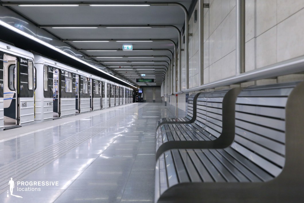 This contemporary metro station features a clean, streamlined design with a monochromatic color palette that enhances its futuristic and minimalist aesthetic. The polished flooring reflects the linear overhead lighting, creating a sense of depth and continuity along the platform. The metal and glass elements contribute to the sleek, industrial ambiance, while the geometric curvature of the ceiling and wall panels adds visual interest. A stationary metro train with open doors extends along the platform, reinforcing the structured, orderly composition of the space. The uncluttered and symmetrical layout makes this location an ideal backdrop for urban transit-themed visuals, emphasizing efficiency and modernity.