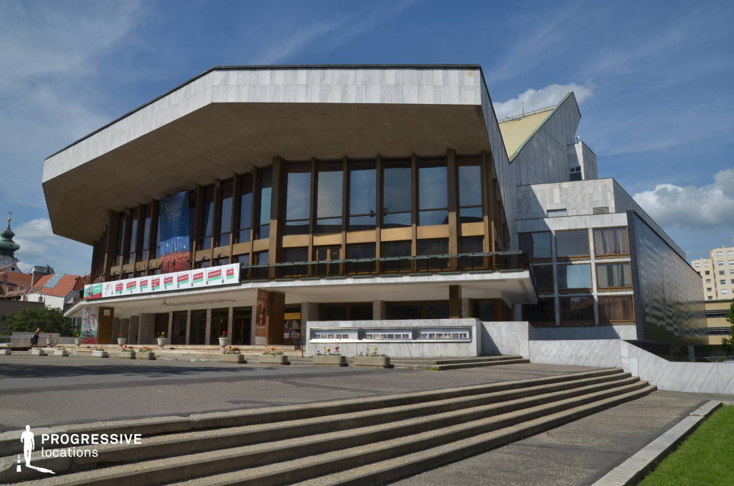 This striking cultural venue exemplifies modernist architecture, featuring sharp angular overhangs, expansive glass facades, and a mix of concrete and marble finishes. The wide staircases and tiered entryway enhance its grandeur, while the geometric window patterns add a dynamic visual rhythm to the structure. The bold, cantilevered roof creates a dramatic presence, making this an ideal location for filming intellectual dramas, political thrillers, or sophisticated urban narratives. The setting conveys a sense of artistic prestige, making it perfect for scenes involving high culture, formal gatherings, or contemporary social commentary.
