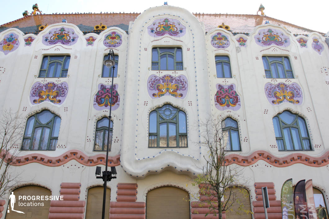 This striking Art Nouveau building features a highly decorative facade adorned with intricate floral motifs, pastel-colored reliefs, and curved architectural forms. The flowing, organic shapes and asymmetrical window designs contribute to the building’s whimsical and artistic character, while the sculpted details and ornate roof elements add depth and vibrancy. The soft color palette, dominated by cream, pink, and lavender hues, enhances its dreamlike quality. This location is ideal for filming period pieces, fantasy narratives, or romantic dramas, offering a visually rich and unconventional backdrop. The elaborate facade provides an excellent setting for stories involving elegance, creativity, or mystery, making it suitable for both historical and surreal cinematic interpretations.