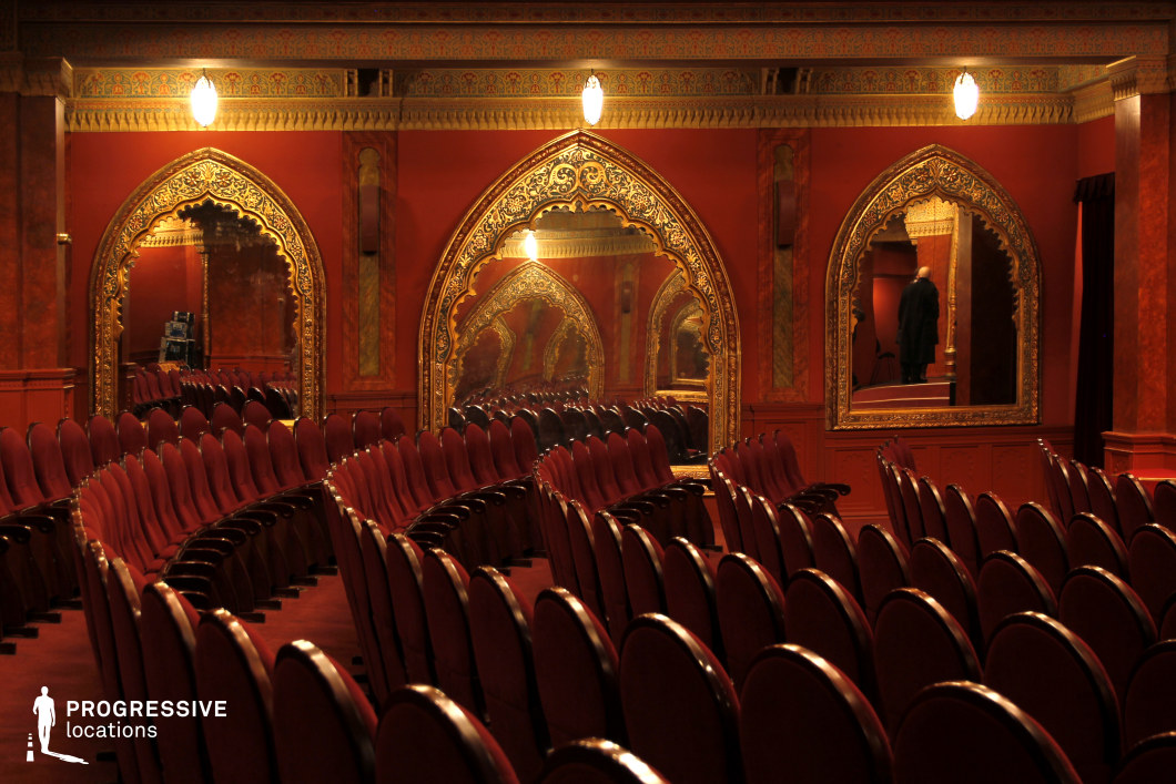 This lavish theater auditorium features deep red hues, arched golden-framed mirrors, and Moorish-inspired architectural details, creating a rich and immersive atmosphere. The rows of plush red velvet seats curve elegantly, enhancing the sense of grandeur and symmetry. The intricate mirrored reflections amplify the space, adding depth and a sense of mystery. The ornate paneling and decorative archways contribute to an exotic, historic ambiance. This setting is ideal for films requiring a luxurious, old-world aesthetic, making it perfect for period dramas, mystery thrillers, or atmospheric noir productions.