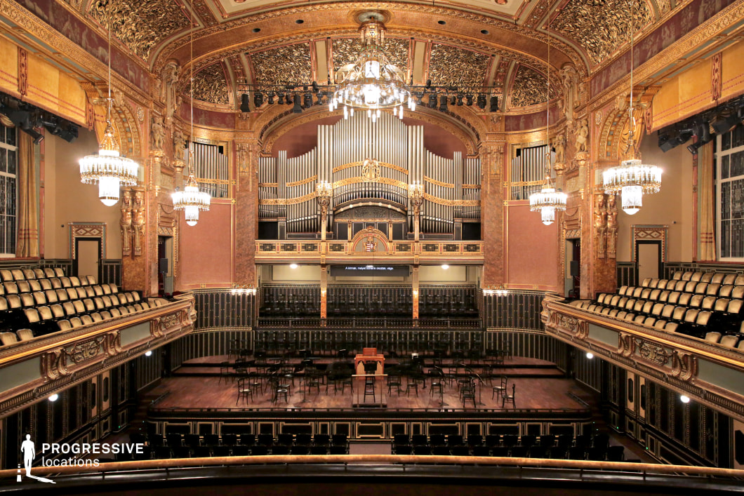 This grand concert hall is a masterpiece of classical architecture, featuring intricate gold detailing, opulent chandeliers, and an imposing pipe organ as the focal point. The high, vaulted ceiling is adorned with elaborate gilded moldings, while the tiered balconies showcase elegant wrought iron railings and plush seating. The wooden stage, framed by decorative panels and statues, enhances the hall’s sense of grandeur. The lighting creates a warm, atmospheric glow, emphasizing the luxurious textures and ornate craftsmanship. This venue is ideal for films requiring a sophisticated and historical setting, such as period dramas, classical music performances, or aristocratic intrigue.