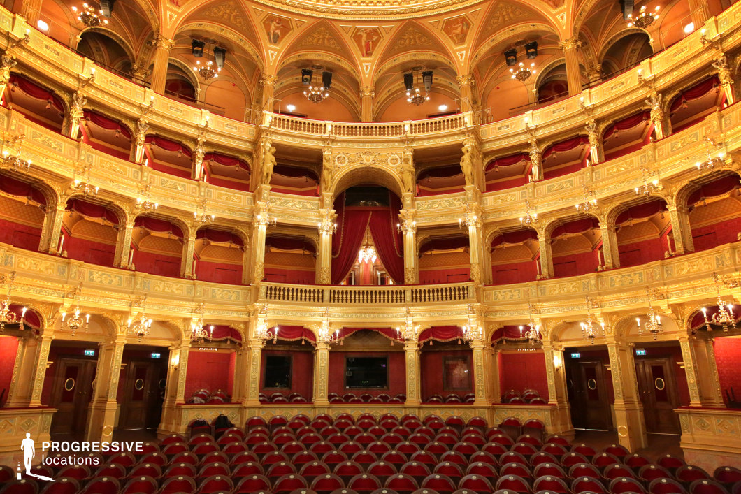 This opulent opera house auditorium showcases a stunning display of classical architecture, with intricate gold detailing, lavish red velvet drapery, and multi-tiered balconies. The arched ceiling is adorned with frescoes and chandeliers, enhancing the grandeur of the space. The symmetrical design and warm lighting create a visually captivating atmosphere, perfect for period dramas, high-society scenes, or classical performance settings. The luxurious ambiance makes it an ideal backdrop for elegant storytelling, refined artistic events, or historically inspired productions.