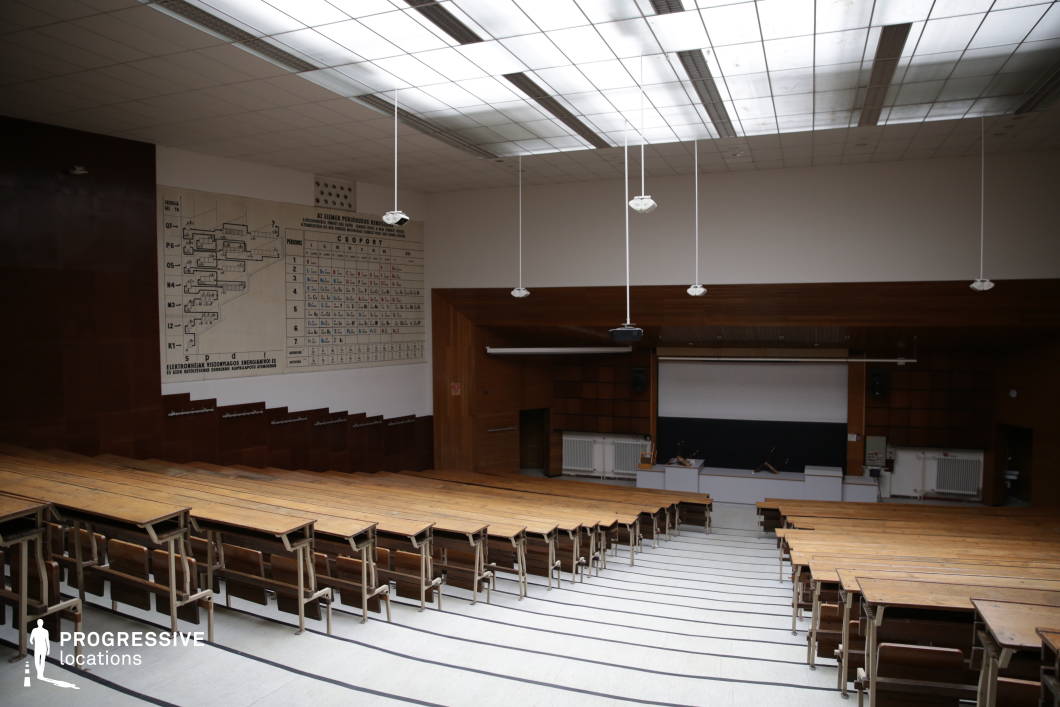 This traditional science lecture hall features tiered wooden seating with integrated writing surfaces, creating a structured academic environment. The large periodic table and electron configuration diagram on the wall emphasize its educational purpose, while the wood-paneled walls add warmth and historical character. A spacious lecturer’s area with a blackboard, projection screen, and laboratory-style demonstration desk ensures versatility for teaching and presentations. The overhead skylights provide natural illumination, making this hall an ideal setting for scientific lectures, academic conferences, or historical educational scenes.