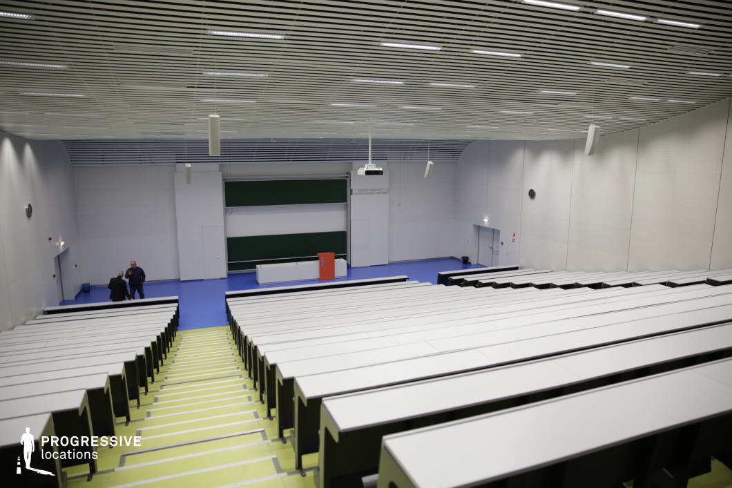 This modern auditorium features tiered seating with sleek white desks and black seating elements, creating a minimalist and professional aesthetic. The wide central staircase with contrasting yellow steps enhances accessibility, while the slatted ceiling with integrated lighting ensures even illumination. A large blackboard and a suspended projector define the lecturer’s area, reinforcing the space’s high-tech educational purpose. The neutral color palette, clean lines, and efficient spatial layout make this venue ideal for large-scale academic lectures, conferences, or corporate presentations requiring a contemporary setting.