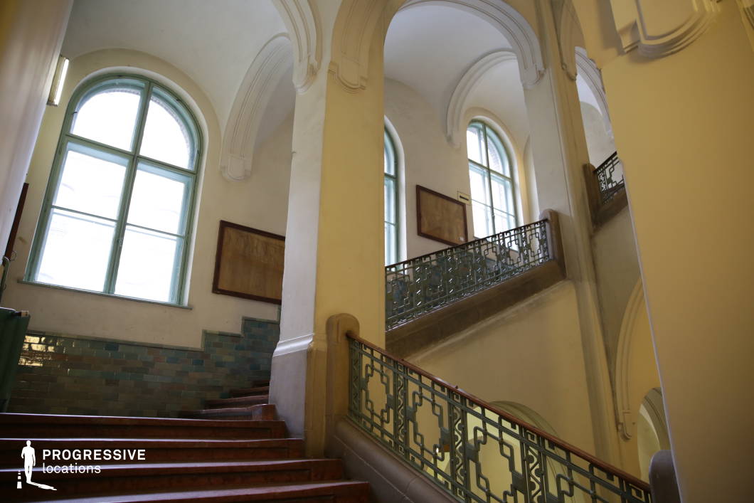 This elegant historic staircase features arched ceilings, decorative wrought-iron railings, and large windows framed in soft green, allowing natural light to enhance the architectural details. The walls incorporate glazed ceramic tiles, adding texture and a subtle contrast to the smooth plastered surfaces. The curved steps and layered landings create a dynamic flow, while intricate molding details emphasize the classical character of the space. The combination of vintage craftsmanship and academic ambiance makes this staircase ideal for settings requiring a refined, old-world institutional aesthetic.