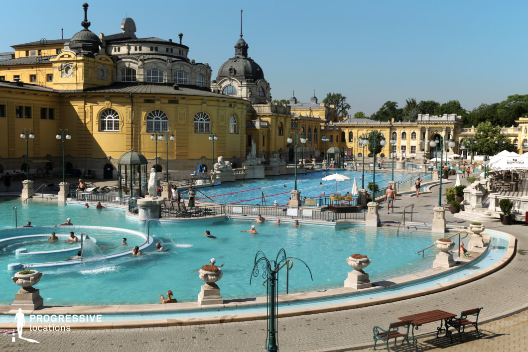 This grand outdoor thermal bath features a sprawling neoclassical complex with ornate yellow facades, domed towers, and arched windows, exuding a sense of historic luxury. The interconnected pools, lined with elegant stone balustrades, fountains, and sculptures, create a visually rich and sophisticated atmosphere. Decorative lampposts and carefully placed greenery enhance the grandeur of the space. The blend of classical architecture and serene water elements makes this location ideal for filming period dramas, travel documentaries, or high-end lifestyle productions.