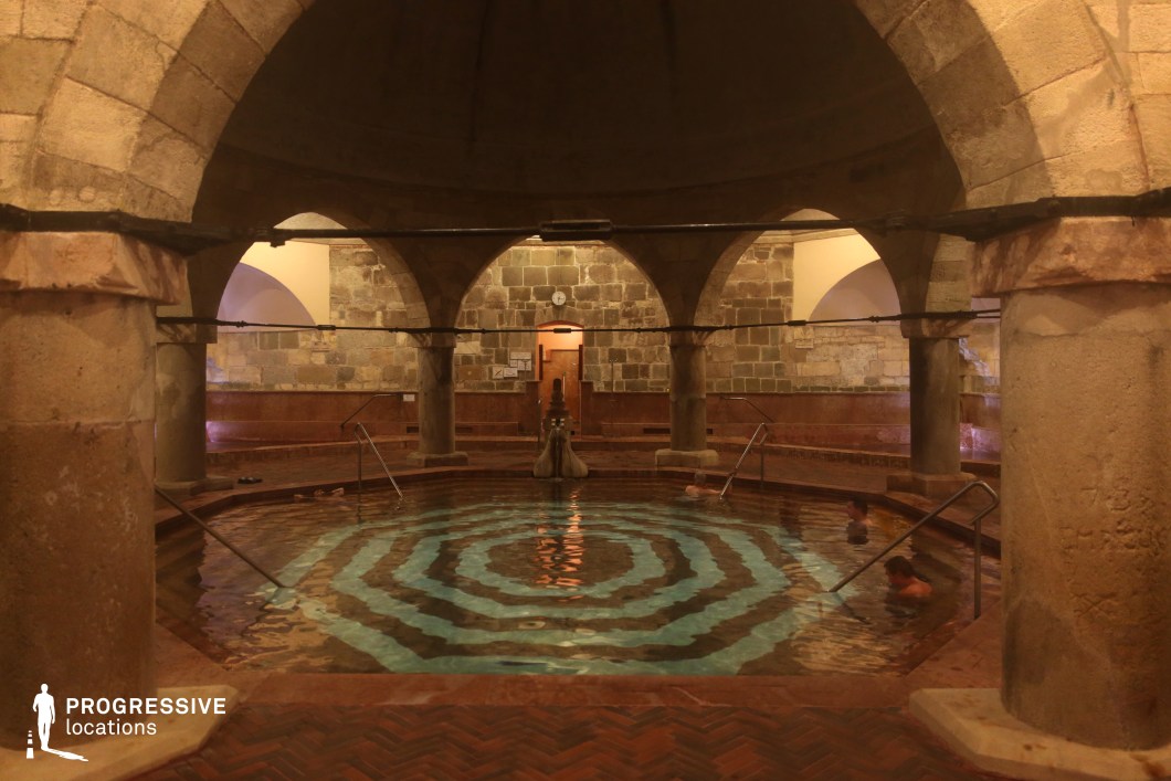 This atmospheric thermal bath features an ancient domed structure supported by robust stone arches, evoking a rich Ottoman-era design. The circular pool is adorned with concentric tile patterns, enhancing the depth and symmetry of the space. The warm-toned stone walls and soft ambient lighting create a mystical and immersive ambiance. The textured masonry and arched alcoves add to the historical authenticity of the setting. This location is ideal for filming historical dramas, period pieces, and cinematic productions requiring an exotic or medieval atmosphere.