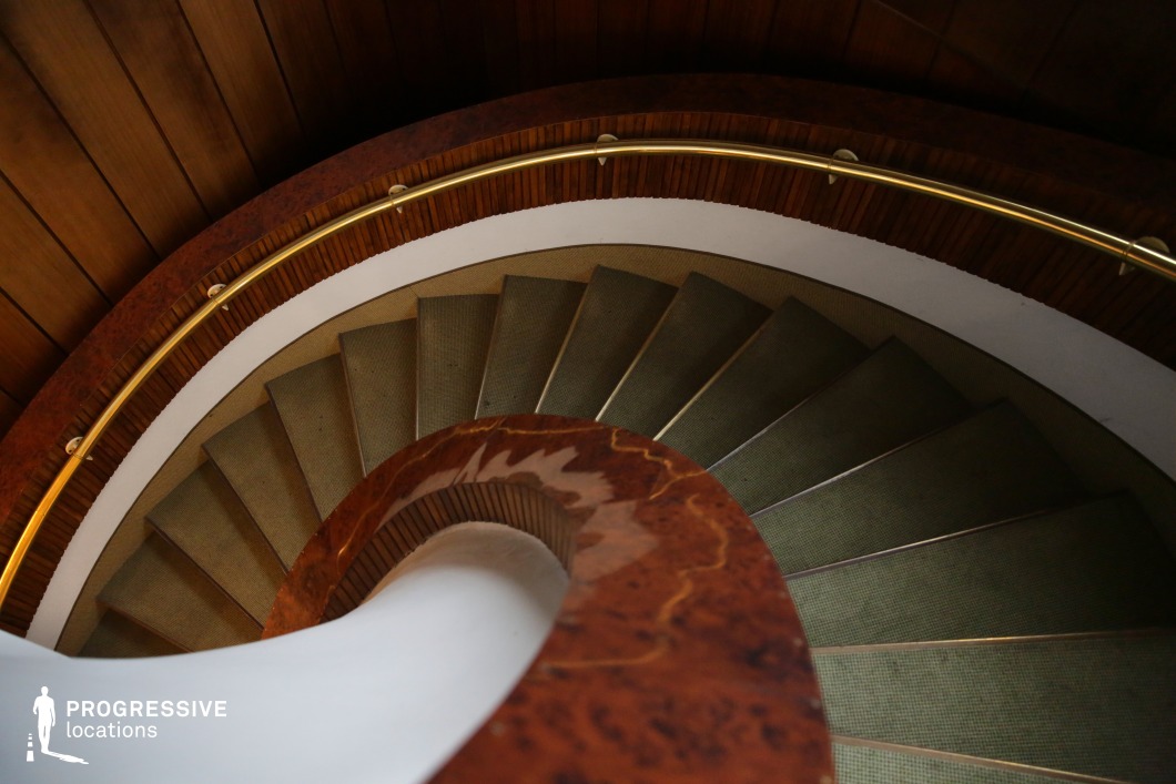 This gracefully curved spiral staircase features a combination of polished wood, warm marble, and a gold-toned railing, creating a sophisticated and timeless aesthetic. The rich textures of the materials enhance the luxurious ambiance, while the soft carpeted steps provide a subtle contrast against the smooth, flowing lines of the banister. The perspective from above emphasizes the staircase’s dynamic geometry, making it an ideal setting for stylish thrillers, psychological dramas, or period films. Its cinematic quality lends itself to scenes of intrigue, suspense, or elegant character introductions.
