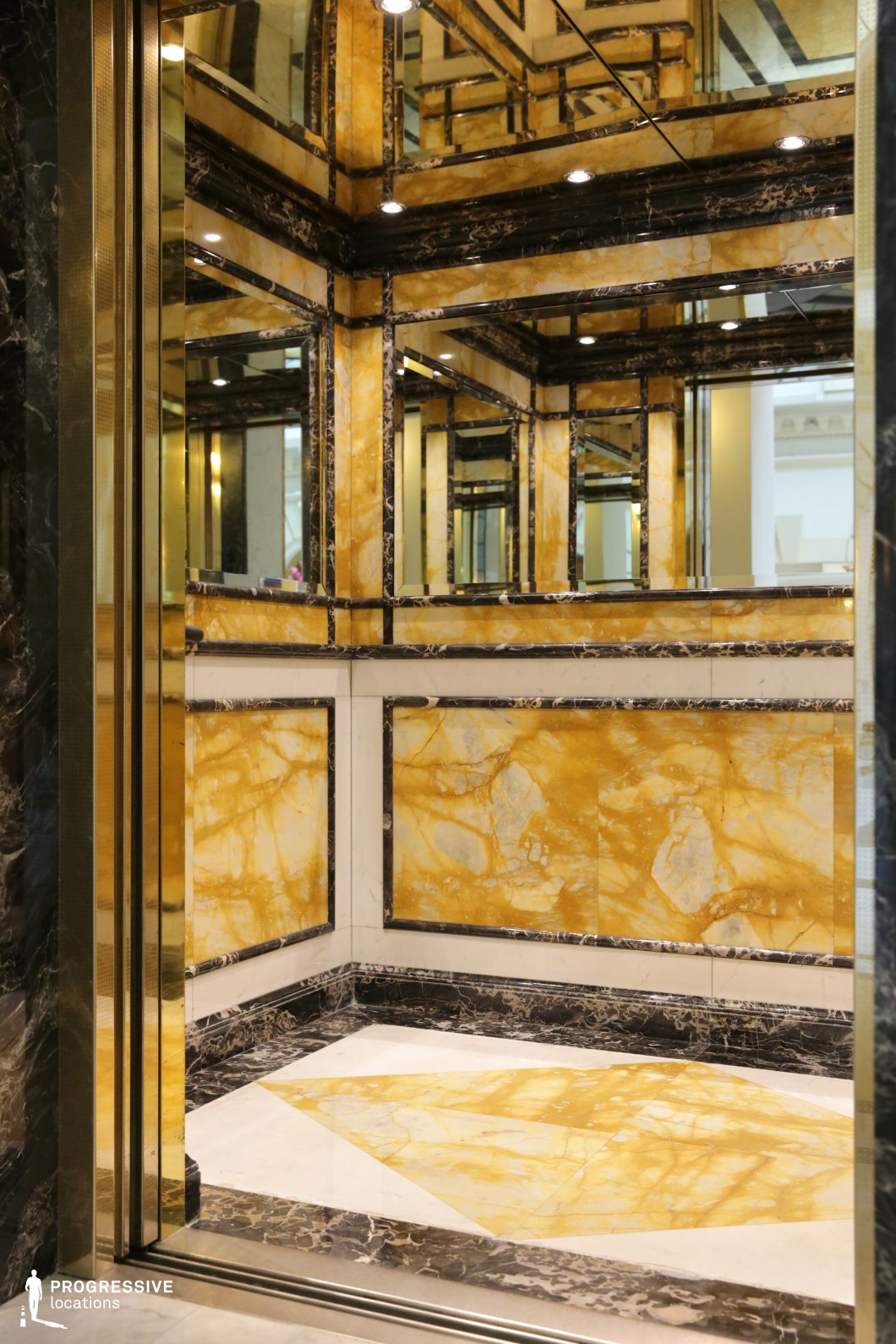 This opulent elevator interior features striking gold-veined marble contrasted with deep black accents, creating a sense of grandeur and refinement. The mirrored panels reflect the intricate geometric patterns, enhancing the illusion of depth and space. Soft recessed lighting adds to the lavish atmosphere, highlighting the polished surfaces. The combination of rich materials and precise symmetry makes this an ideal setting for high-stakes dramas, crime thrillers, or stylish noir films, offering a visually compelling backdrop for moments of tension, secrecy, or luxurious exclusivity.