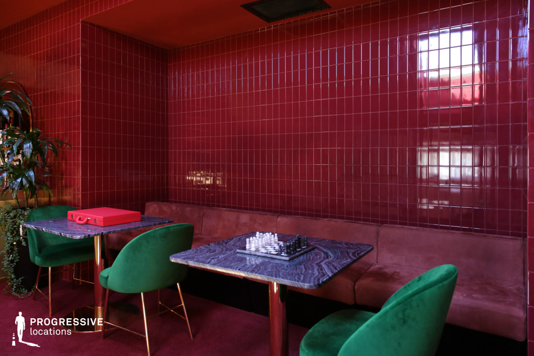 This bold lounge space features glossy red tiled walls, a matching plush carpet, and a velvet-upholstered bench, creating a dramatic and intimate setting. Deep green velvet chairs with gold legs contrast beautifully against the rich red tones, while dark marble-top tables add an element of sophistication. The combination of reflective surfaces, luxurious textures, and bold color choices makes this an ideal filming location for vintage-inspired dramas, neo-noir thrillers, or stylish art-house productions that require a moody and atmospheric backdrop.