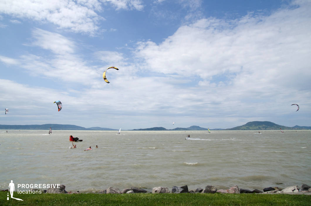 This expansive lakeside view features a wide, breezy water surface framed by grassy and rocky foregrounds, with gentle hills rising on the opposite shore. The open, uninterrupted horizon and dynamic movement on the water offer a sense of freedom and energy. Ideal for filming sports-related content, summer leisure scenes, or outdoor lifestyle segments, this location also suits drama or romance genres that require an airy, spacious lakeside setting with a natural yet energetic ambiance.