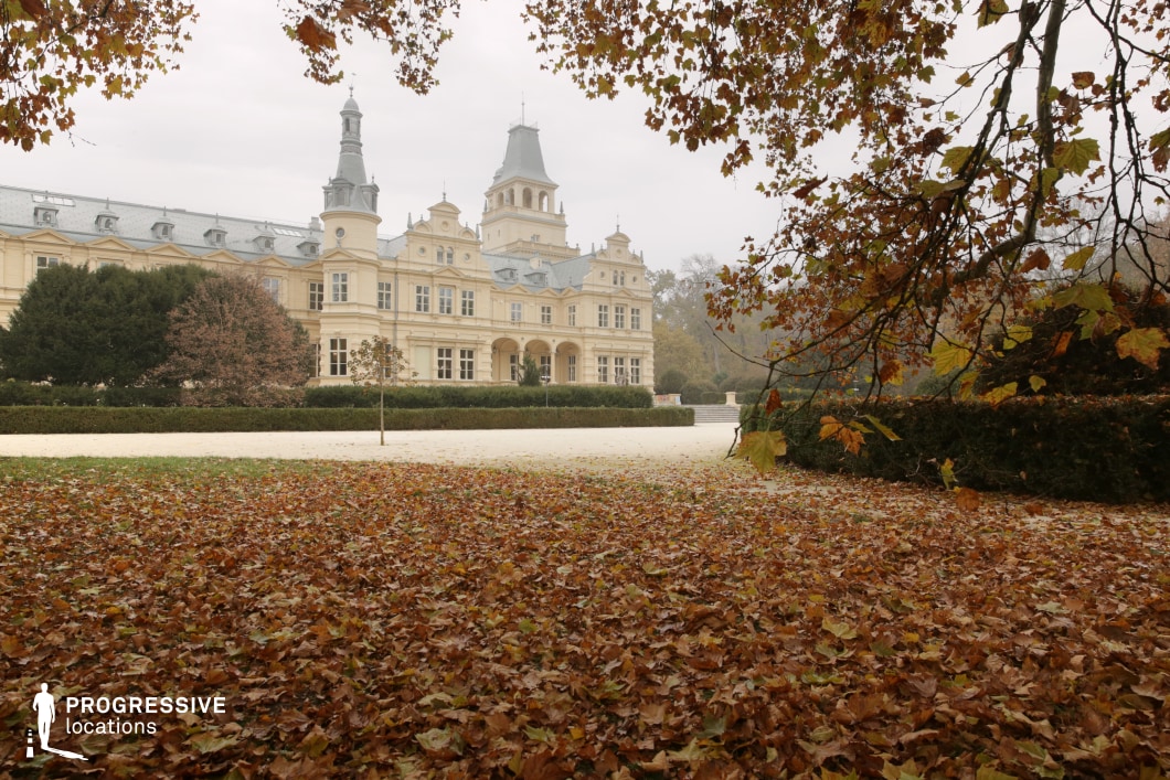 This stately château features an elegant symmetrical façade with intricate detailing, multiple towers, and a grand arched entrance, evoking a sense of aristocratic grandeur. The light-colored exterior is adorned with decorative moldings, dormer windows, and steeply pitched roofs, reflecting a blend of classical and baroque architectural influences. The château is set within an expansive landscaped estate, framed by neatly trimmed hedges and a wide gravel pathway leading toward the entrance. This location is ideal for filming period dramas, historical narratives, and mystery or romance films, providing a regal and sophisticated setting for scenes involving intrigue, nobility, or high society.