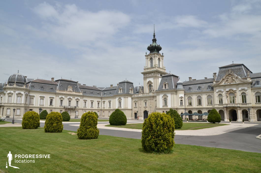  This image showcases a magnificent Baroque-style palace with an expansive, manicured garden in the foreground. The symmetrical facade is adorned with elaborate sculptural details, arched windows, and a central tower topped with an ornate spire. The slate-gray mansard roof and domed corner pavilions enhance the palace’s regal presence. The neatly trimmed shrubs and curved pathways contribute to the estate’s refined aesthetic. This location is ideal for filming period dramas, historical romances, or aristocratic narratives, offering a stately and sophisticated setting for scenes of diplomacy, grandeur, or high society intrigue.