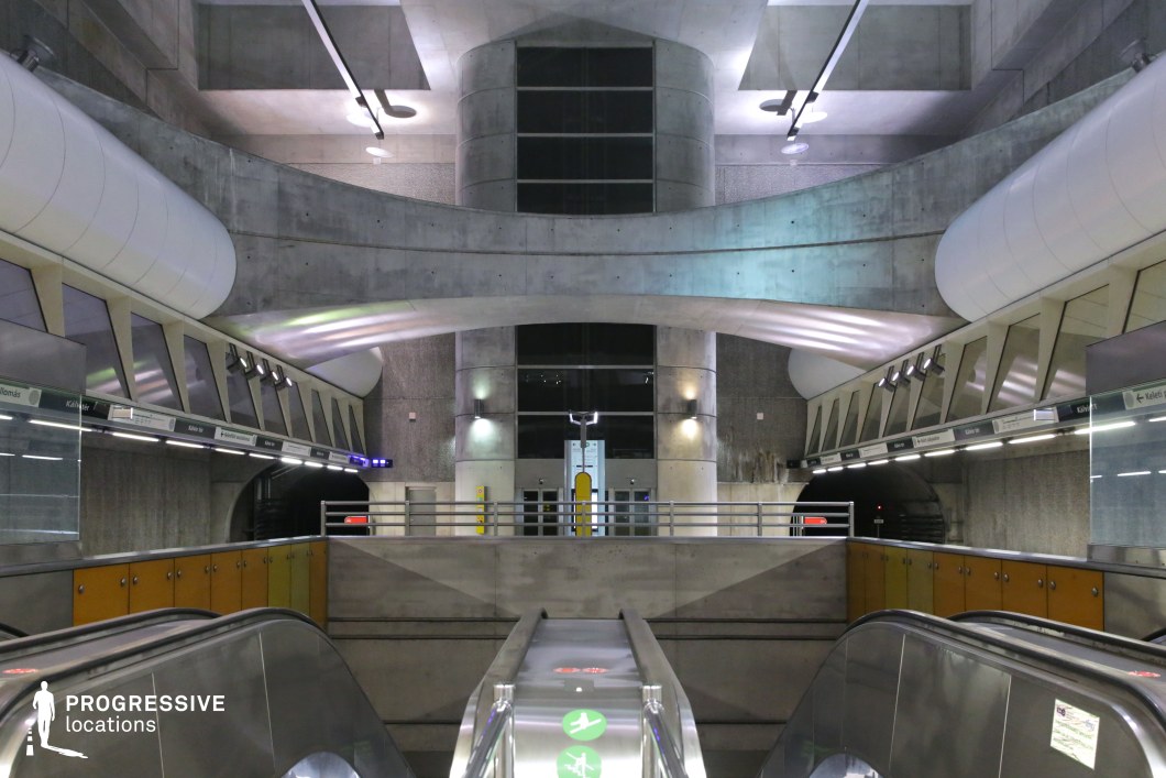 This underground station features an imposing concrete structure with curved architectural elements that seamlessly blend industrial and futuristic aesthetics. The dominant use of exposed concrete is complemented by geometric shapes, metal railings, and smooth, curved white panels that enhance the station's modernity. The overhead lighting casts a soft glow on the surfaces, emphasizing the depth and scale of the space. The symmetrical composition, including escalators and tunnels, creates a sense of movement and dynamism. This location is ideal for sci-fi or dystopian settings, providing a sleek yet brutalist backdrop for cinematic storytelling.