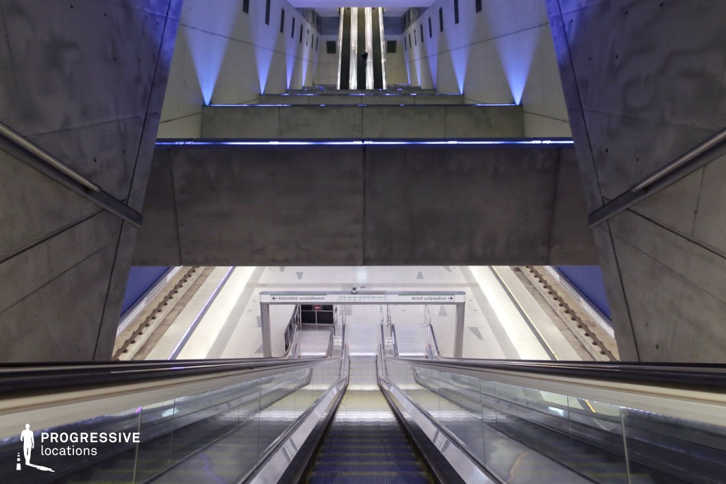This striking underground station features a dramatic interplay of raw concrete geometry and moody blue accent lighting. The long, mirrored escalators extend into the distance, flanked by towering angular walls that emphasize the space’s modern and industrial aesthetic. The use of layered platforms and overhanging beams creates depth, while the cool-toned illumination adds a futuristic ambiance. This location is ideal for cinematic sequences, sci-fi productions, or projects requiring a sleek, dystopian transit setting.