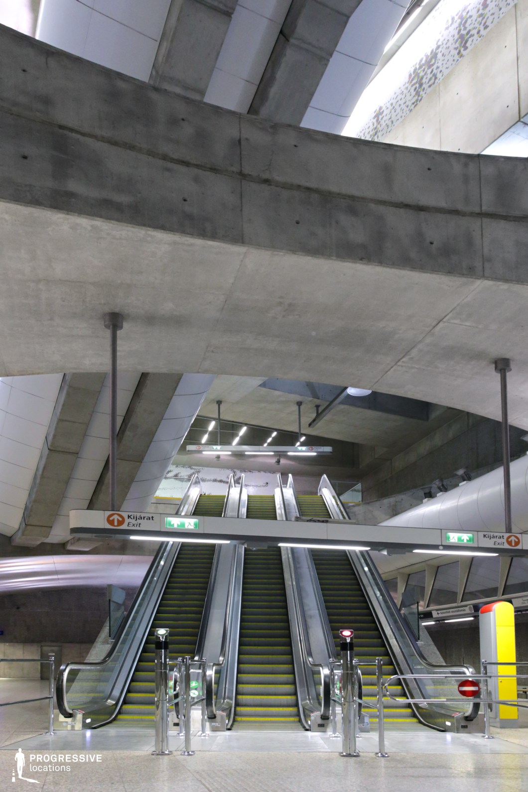 This striking urban space showcases a monumental escalator system encased in raw concrete and industrial metal finishes. Overhead, sweeping concrete beams intersect with curved, white paneling, giving the architecture a futuristic, almost sci-fi-like atmosphere. The composition emphasizes symmetry, with clean lines and geometric patterns guiding the eye upward. Illuminated signage and sleek lighting fixtures enhance the modern aesthetic, making this location ideal for dystopian, cyberpunk, or high-tech cinematic settings.