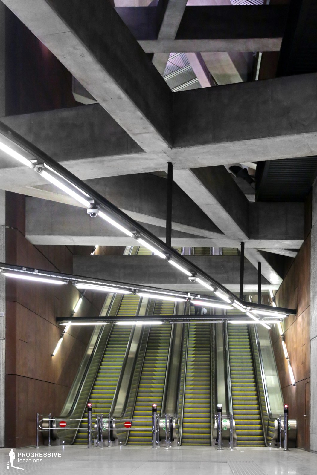 This modern subway station features a striking geometric design with expansive concrete beams and bright industrial lighting that highlights the sharp angles of the space. Central escalators lead the viewer’s gaze upward, flanked by metallic barriers. The combination of concrete surfaces and metallic elements, along with the spacious layout, creates a futuristic, industrial atmosphere, making it ideal for filming urban, sci-fi, or action scenes.