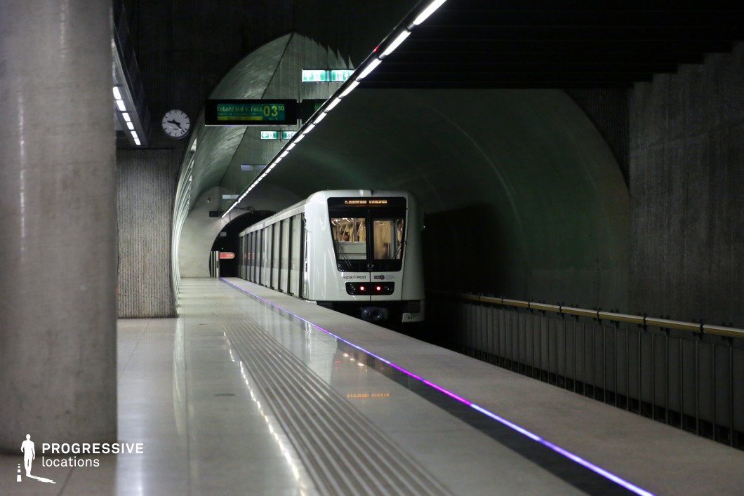 This metro station features a distinctive arched tunnel design, with smooth concrete walls and a dimly lit atmosphere that enhances its industrial and futuristic feel. The sleek metro train contrasts with the textured surfaces of the platform, while the reflective tiled flooring amplifies the ambient lighting, including subtle neon-like edge highlights. Vertical columns add structural depth, leading the eye toward the curved tunnel opening in the background. The symmetrical lighting along the ceiling and train tracks further accentuates the station’s geometric precision. This setting is ideal for filming sci-fi, thriller, or dystopian narratives, offering a visually striking blend of minimalism and industrial modernity.