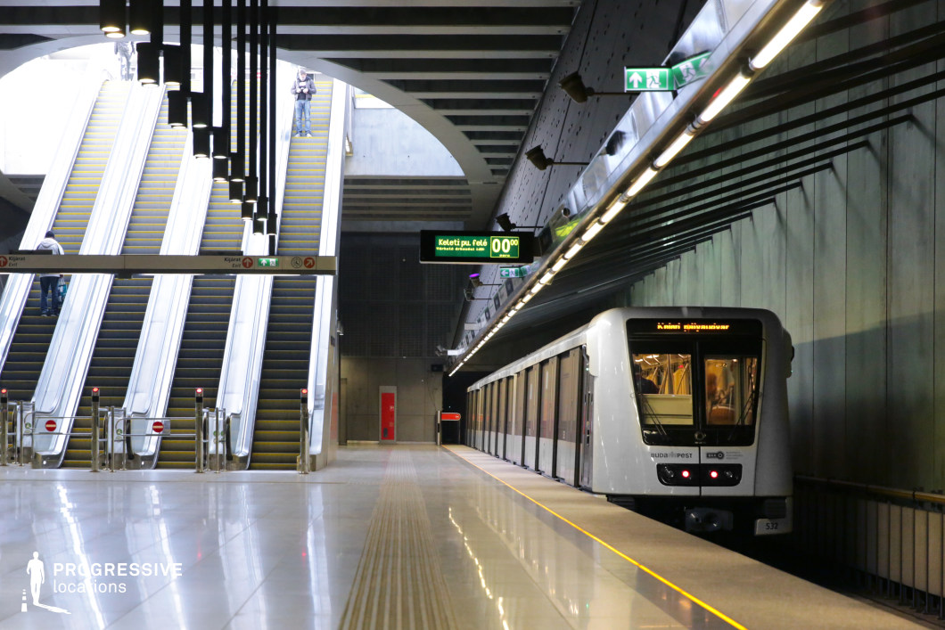 This metro station blends industrial minimalism with modern functionality, featuring polished flooring, metallic walls, and a high ceiling structured with dark steel beams. The large escalators ascend towards an open space where natural light filters through, contrasting with the artificial lighting along the platform. The sleek, silver metro train complements the station’s streamlined design, with its reflective surfaces enhancing the futuristic atmosphere. The geometric ceiling pattern and suspended lighting fixtures create strong visual lines, adding depth and dimension. This location is ideal for filming sci-fi, cyberpunk, thriller, or high-tech espionage scenes, offering a striking mix of industrial precision and urban modernity.