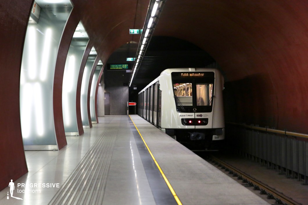 This image showcases a sleek subway platform with curved red walls lit by integrated lighting, creating a striking contrast with the smooth, polished flooring. The minimalist design, with its clean lines and spacious feel, gives the space a modern, futuristic atmosphere. The environment’s industrial yet sleek aesthetic makes it ideal for futuristic, thriller, or science fiction films, providing a visually captivating backdrop for dynamic and cinematic scenes.