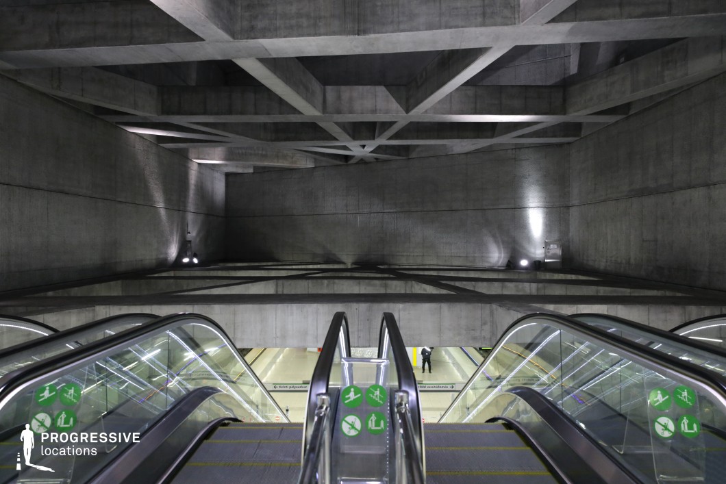 This metro station features a striking brutalist architectural design with raw concrete walls and an intricate ceiling structure composed of intersecting geometric beams. The descending escalators, framed by sleek glass railings, lead into a cavernous underground space, emphasizing depth and scale. The dim artificial lighting casts dramatic shadows on the concrete surfaces, enhancing the location’s stark, industrial atmosphere. The rigid geometry and cold materials create a dystopian, high-tech ambiance, making this an excellent filming location for sci-fi, cyberpunk, thriller, or espionage genres.