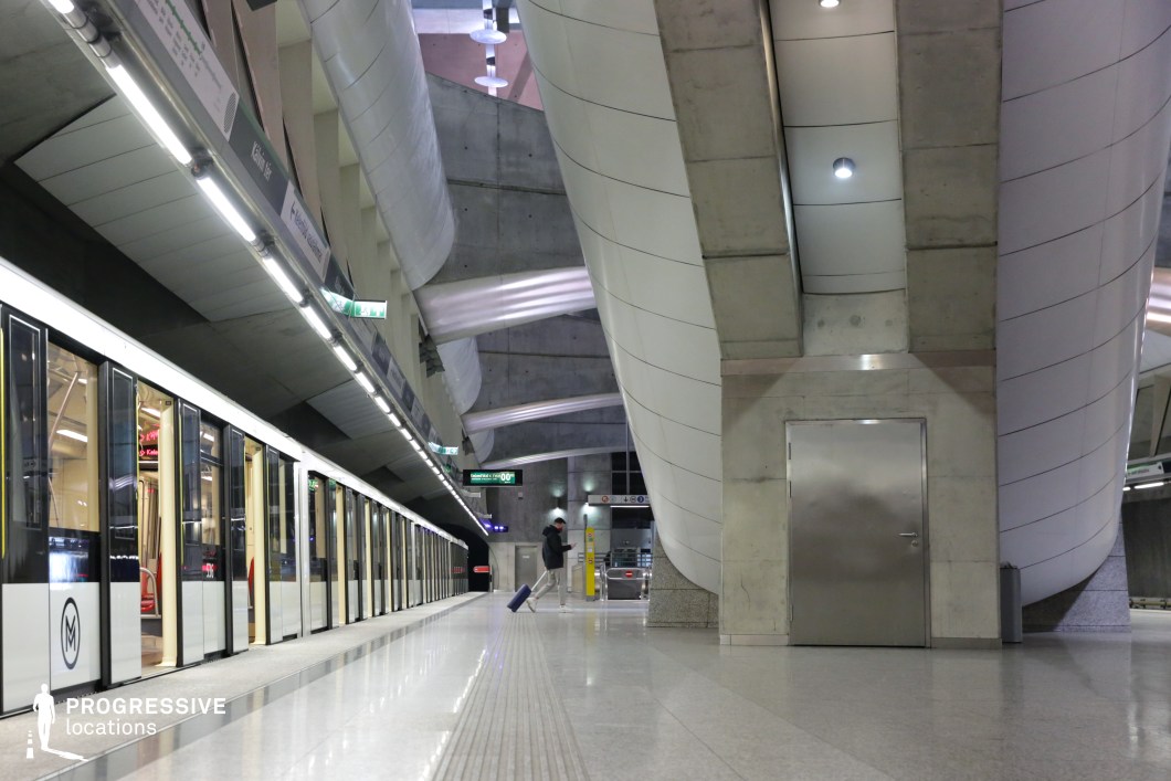 This metro platform features a sleek, industrial aesthetic dominated by raw concrete and smooth, curved white panels. The ceiling is punctuated by embedded lighting that enhances the station’s contemporary look. A train with minimalist black-and-white doors aligns with the platform, reinforcing the modern, streamlined feel. The polished floor reflects the surrounding architecture, adding depth and symmetry. The combination of rigid geometric forms and sweeping curves creates a dynamic environment ideal for cinematic scenes requiring a futuristic or high-tech urban setting.