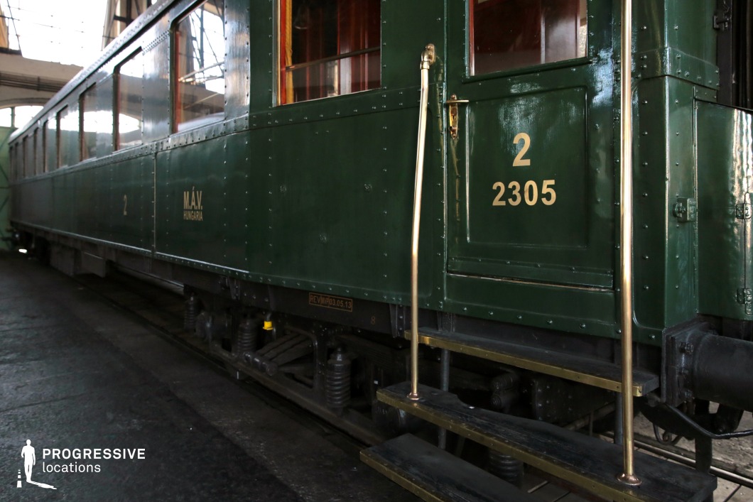 This vintage railway carriage, painted in deep green with gold lettering, showcases classic riveted metal construction and polished brass railings. The sturdy wooden steps lead to a small platform, reinforcing the train’s early 20th-century design. Large rectangular windows with warm wooden frames offer a glimpse into the interior, adding to the nostalgic charm. The glossy exterior and detailed craftsmanship make this an ideal setting for period dramas, historical thrillers, or classic railway travel narratives requiring an authentic and refined train environment.