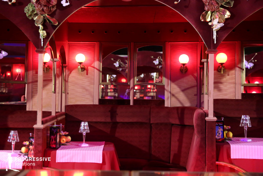 This intimate, vintage-style lounge exudes a sultry and theatrical atmosphere with deep red velvet booths, mirrored walls, and soft, glowing wall sconces casting a warm light. The arched ceiling and decorative elements add an air of classic elegance, while the plush upholstery and reflective surfaces enhance the depth and moodiness of the setting. Small, candle-lit tables with carefully arranged details contribute to the sense of exclusivity. This location is ideal for noir-inspired films, cabaret-themed productions, or scenes set in an upscale yet mysterious nightlife venue, offering a visually rich and immersive backdrop.