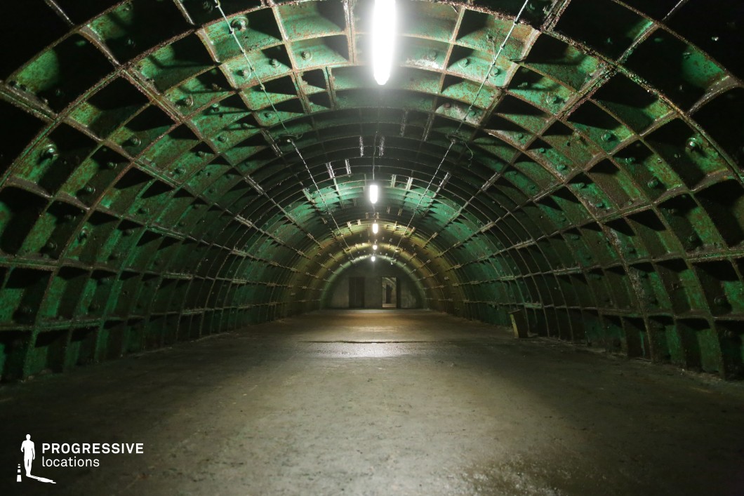 Green steel-framed tunnel with fluorescent lighting, an industrial film and photography location with rhythmic symmetry.